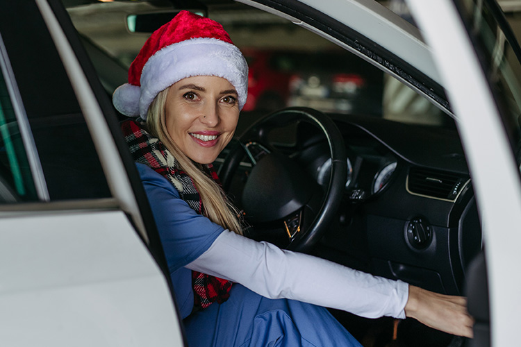 A frontline worker wearing a Santa hat, opening a car door and smiling