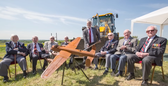 A group photo of the eight veterans of Bomber Command sat behind a model fighter jet.