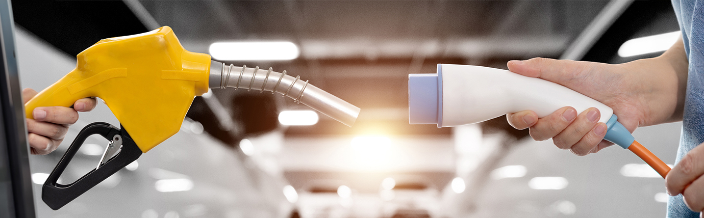 A fuel nozzle and EV charger facing one another, each being held by a person'.