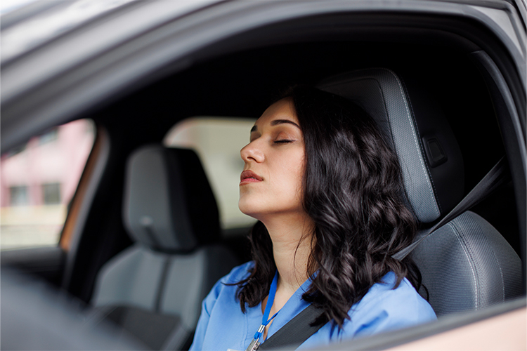A woman reflecting on her day while being sat in the driver's seat of her car