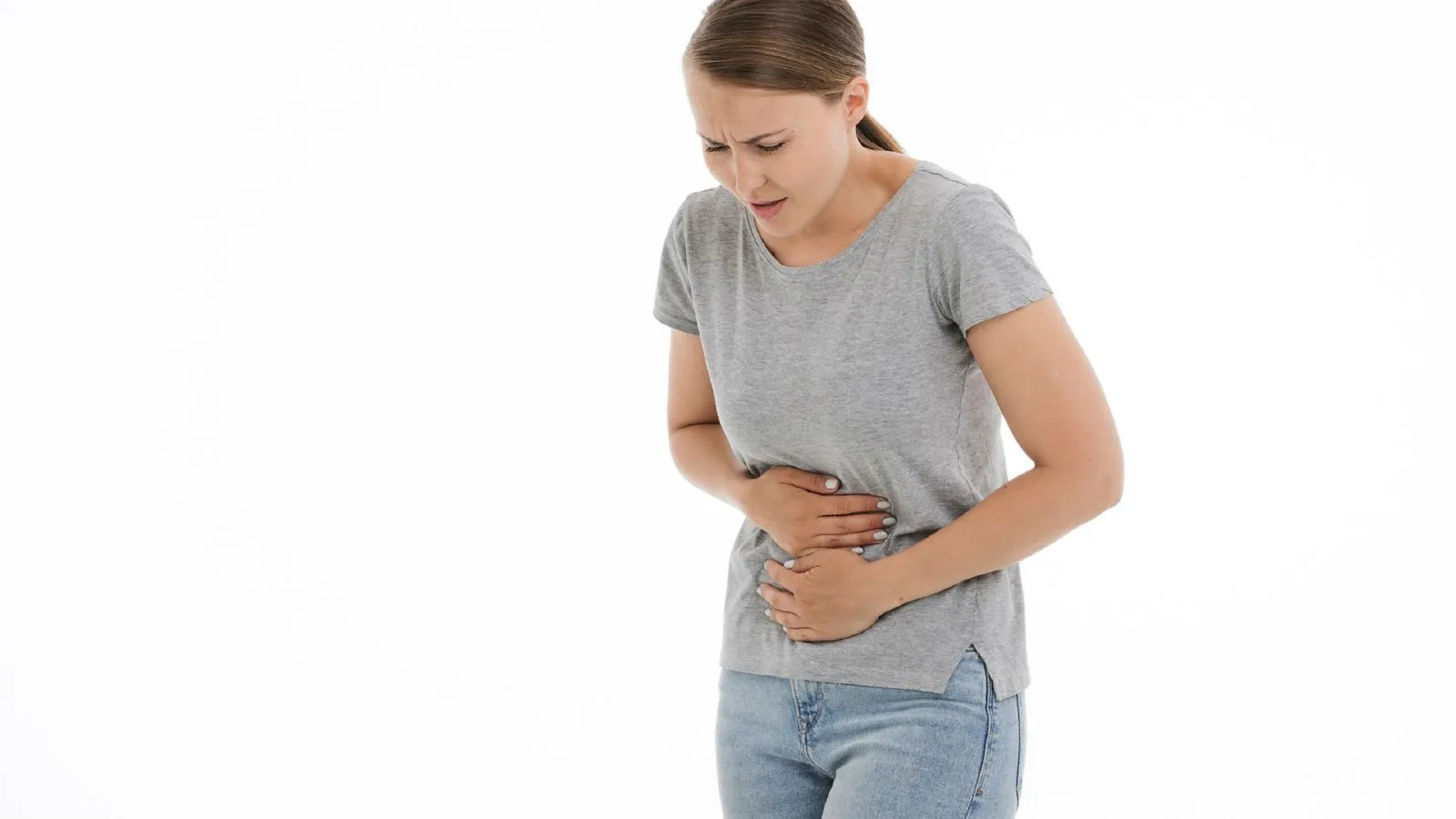 Frau in grauem Tshirt hält sich mit schmerzverzerrtem Gesicht den Bauch.