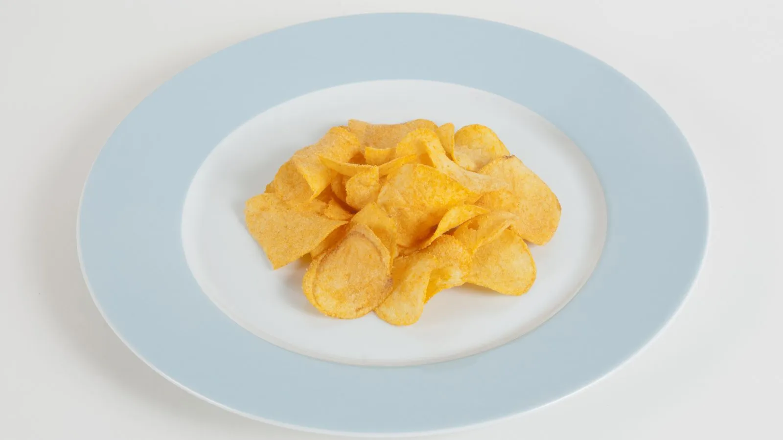 Auf einem weissen Teller mit blauem Rand liegt ein Häufchen Pommes Chips