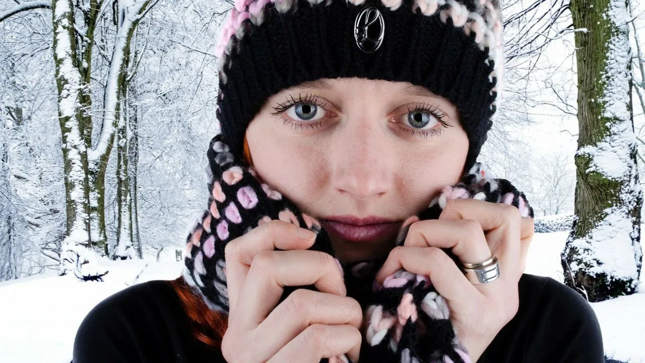 Eine Frau steht in einem verschneiten Wald, sie trägt Schal und Mütze