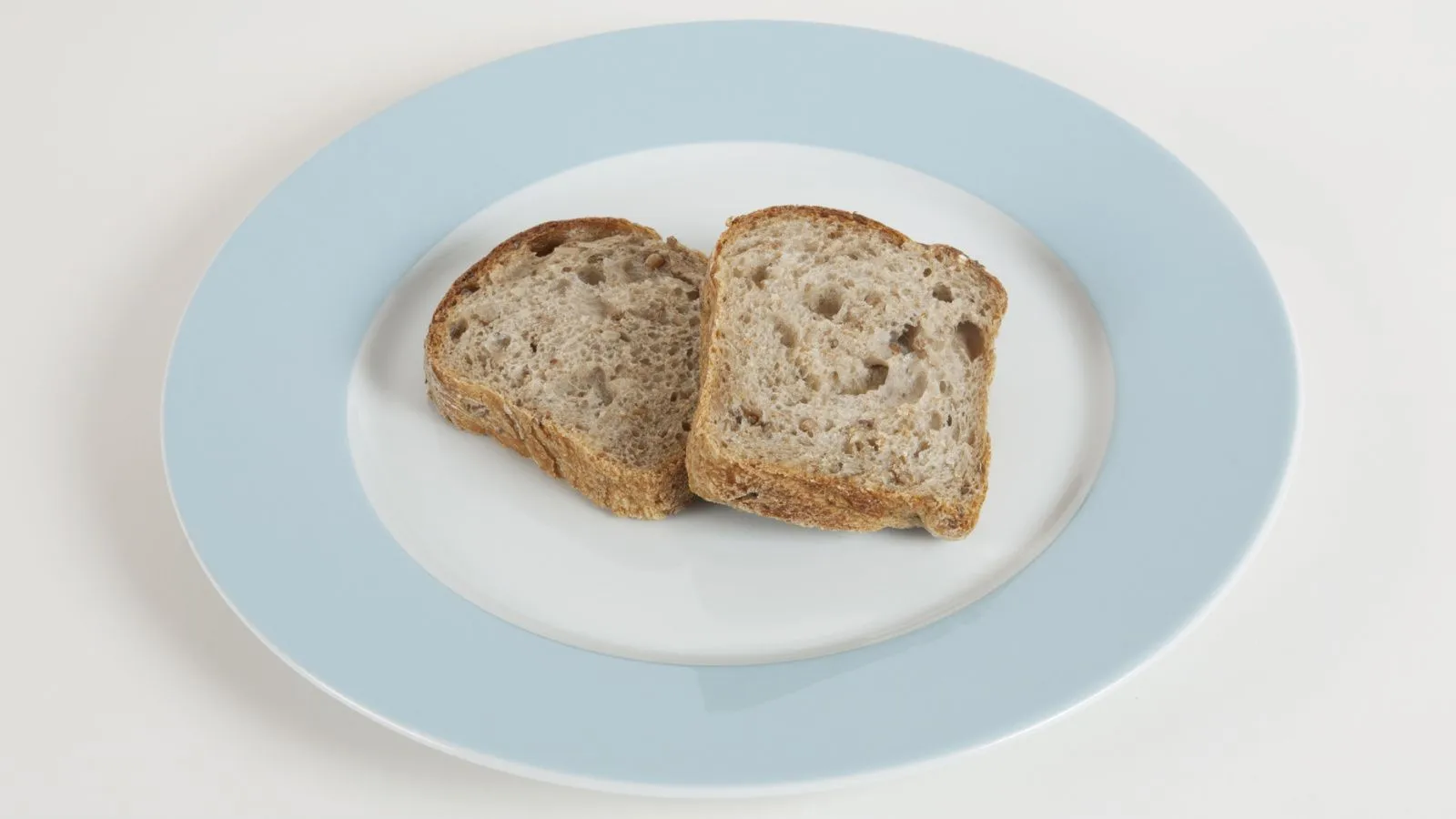 Zwei Scheiben Vollkornbrot liegen auf einem weissen Teller mit blauem Rand