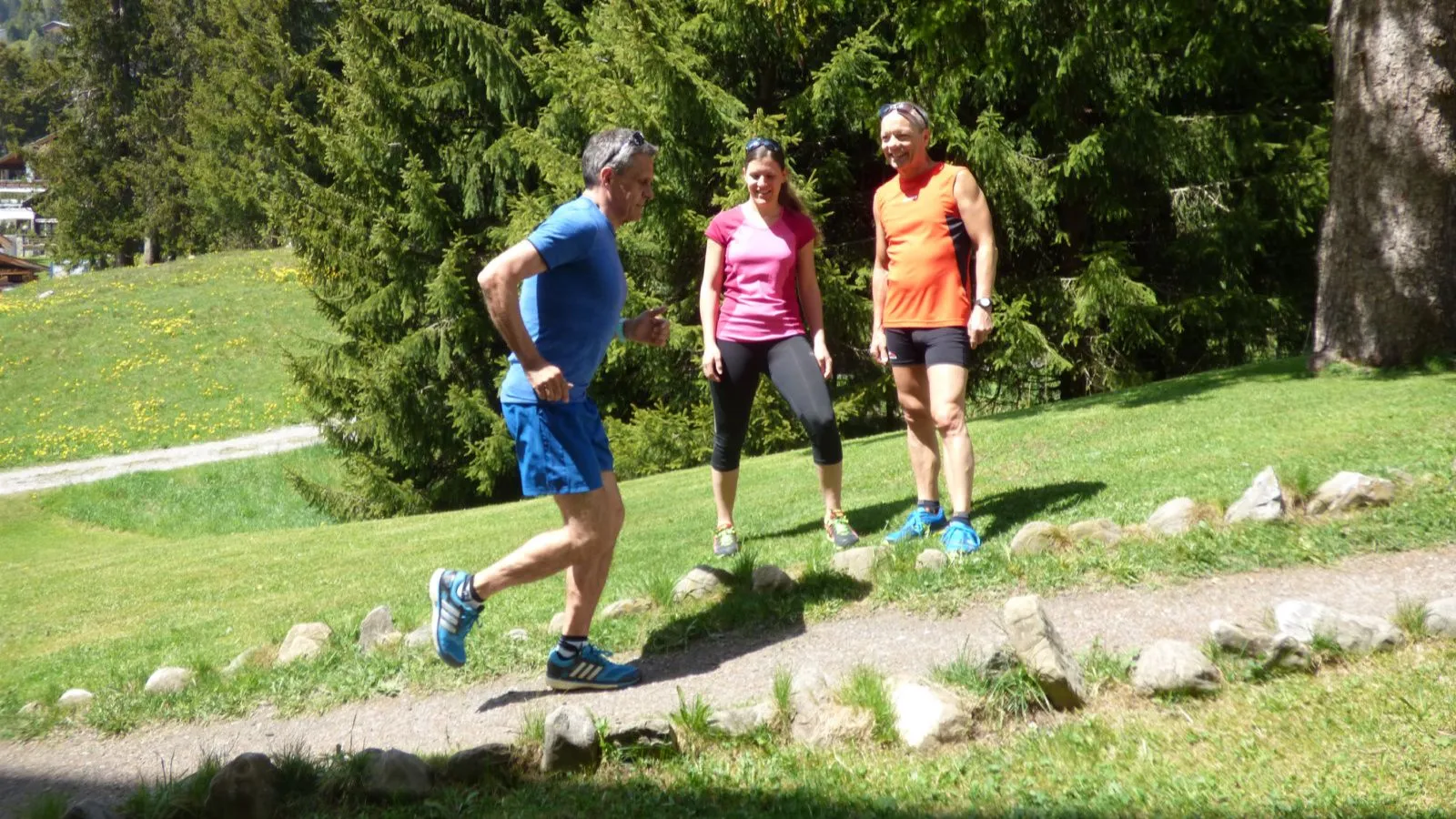 Mann in blauem Sportdress läuft bergauf, zwei andere sehen zu.