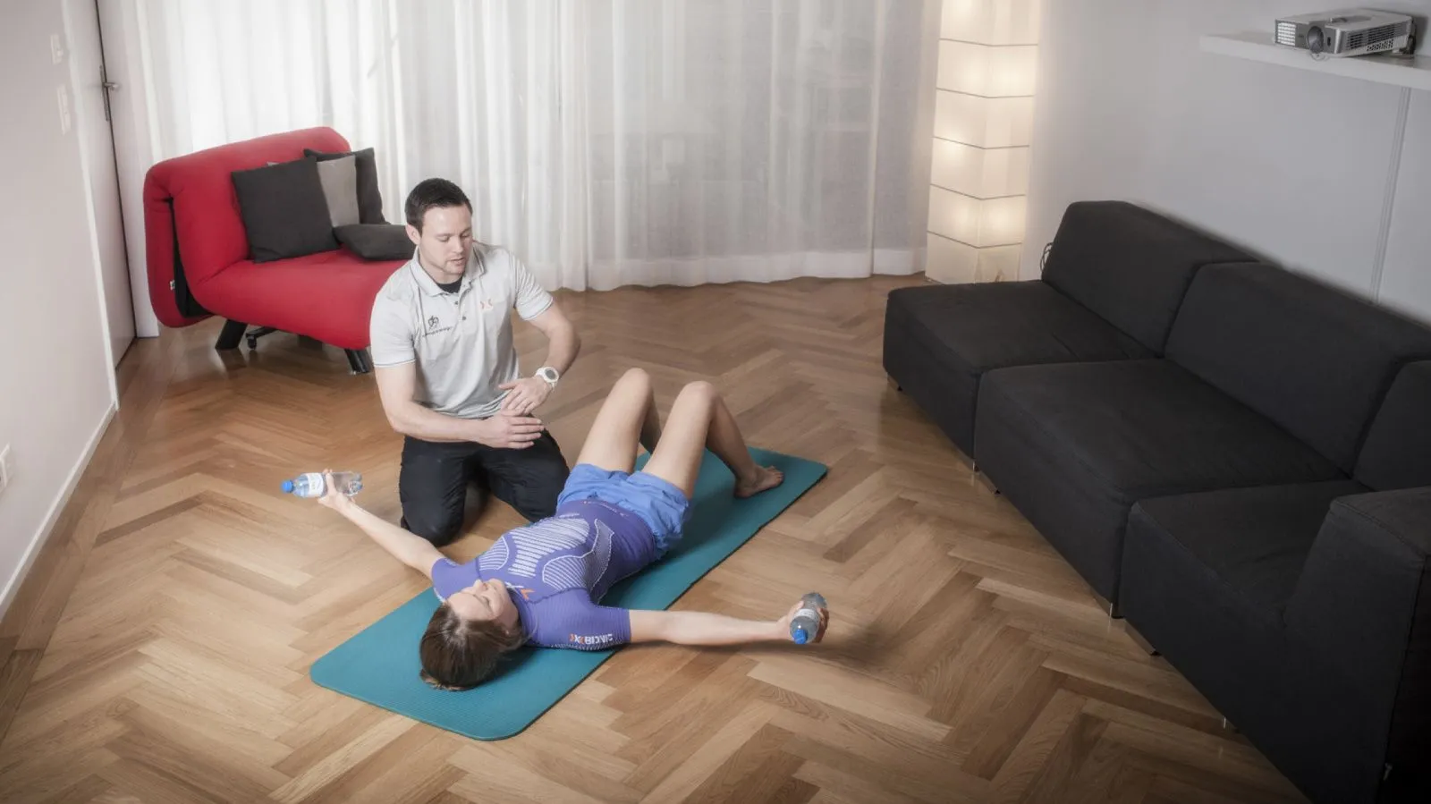 Fitnessschülerin liegt auf Matte, je eine Petflasche in den Händen, die sie anhebt. 