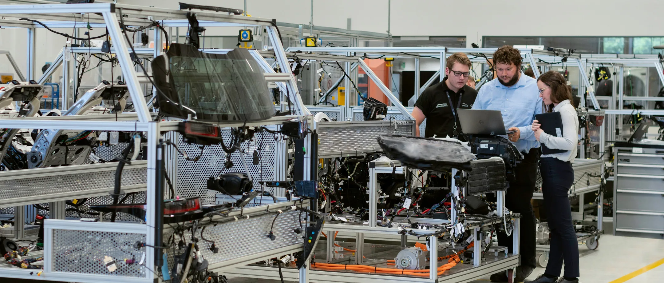 Trois personnes autour d'un ordinateur portable dans un atelier de prototypage automobile.
