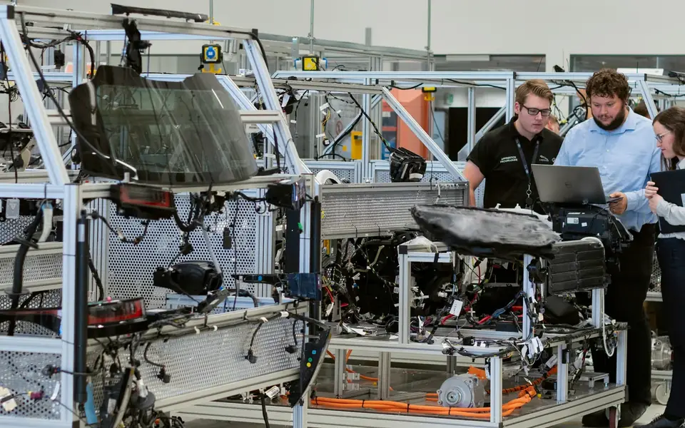 Trois personnes autour d'un ordinateur portable dans un atelier de prototypage automobile.
