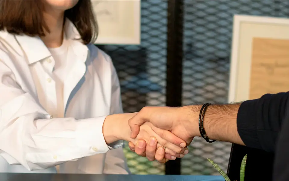 Une poignée de main entre deux personnes de part et d'autre d'une table, dans un bureau.