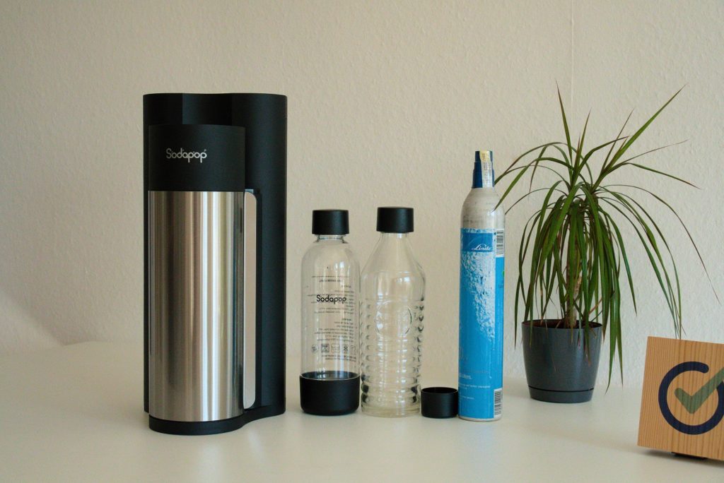 Sodapop neben 2 PET Flaschen, CO2-Zylinder, Pflanze und Holzblock mit testit-Logo