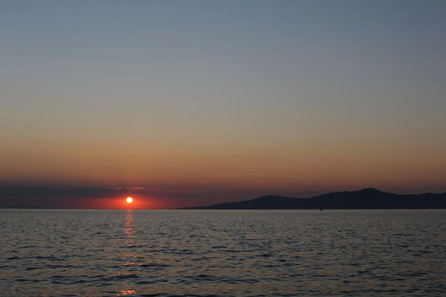 The sun setting over the sea, the sky shading from orange to blue