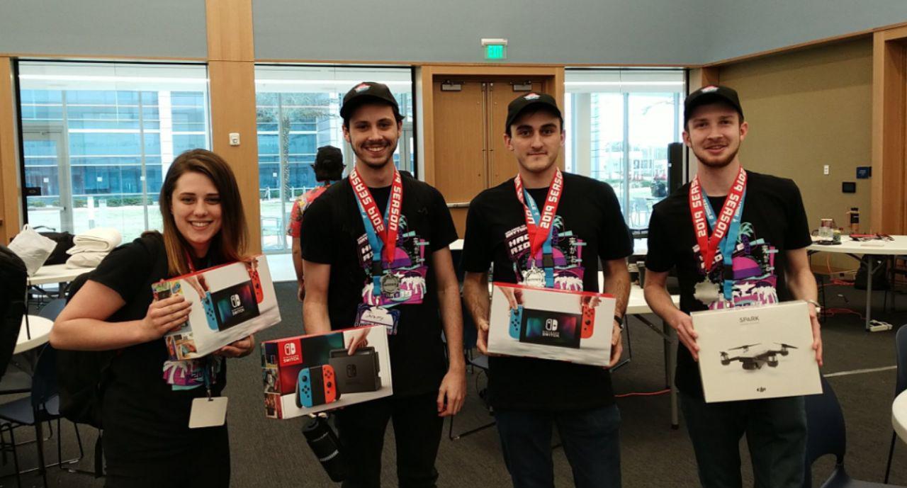 four college students stand sleep deprived, holding their trophies