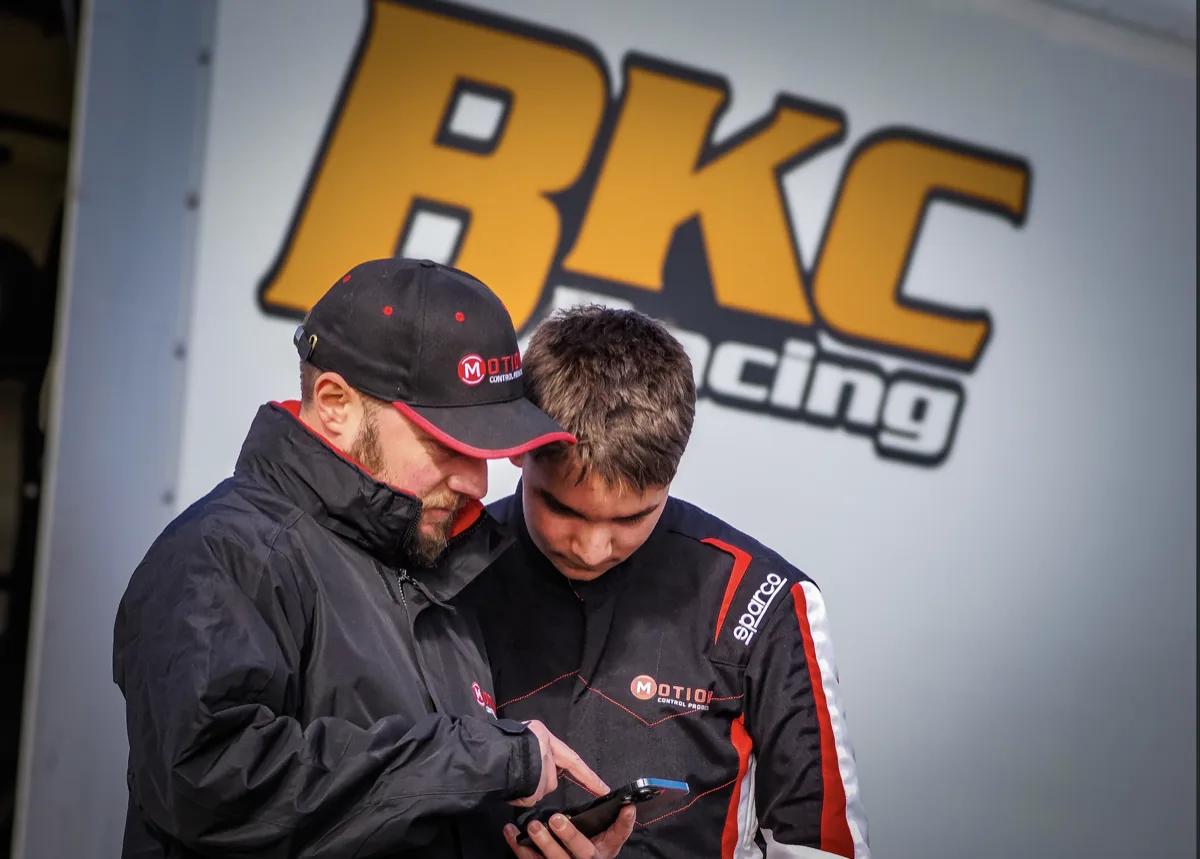 Father and son reviewing karting telemetry data on a phone trackside at RKC Racing