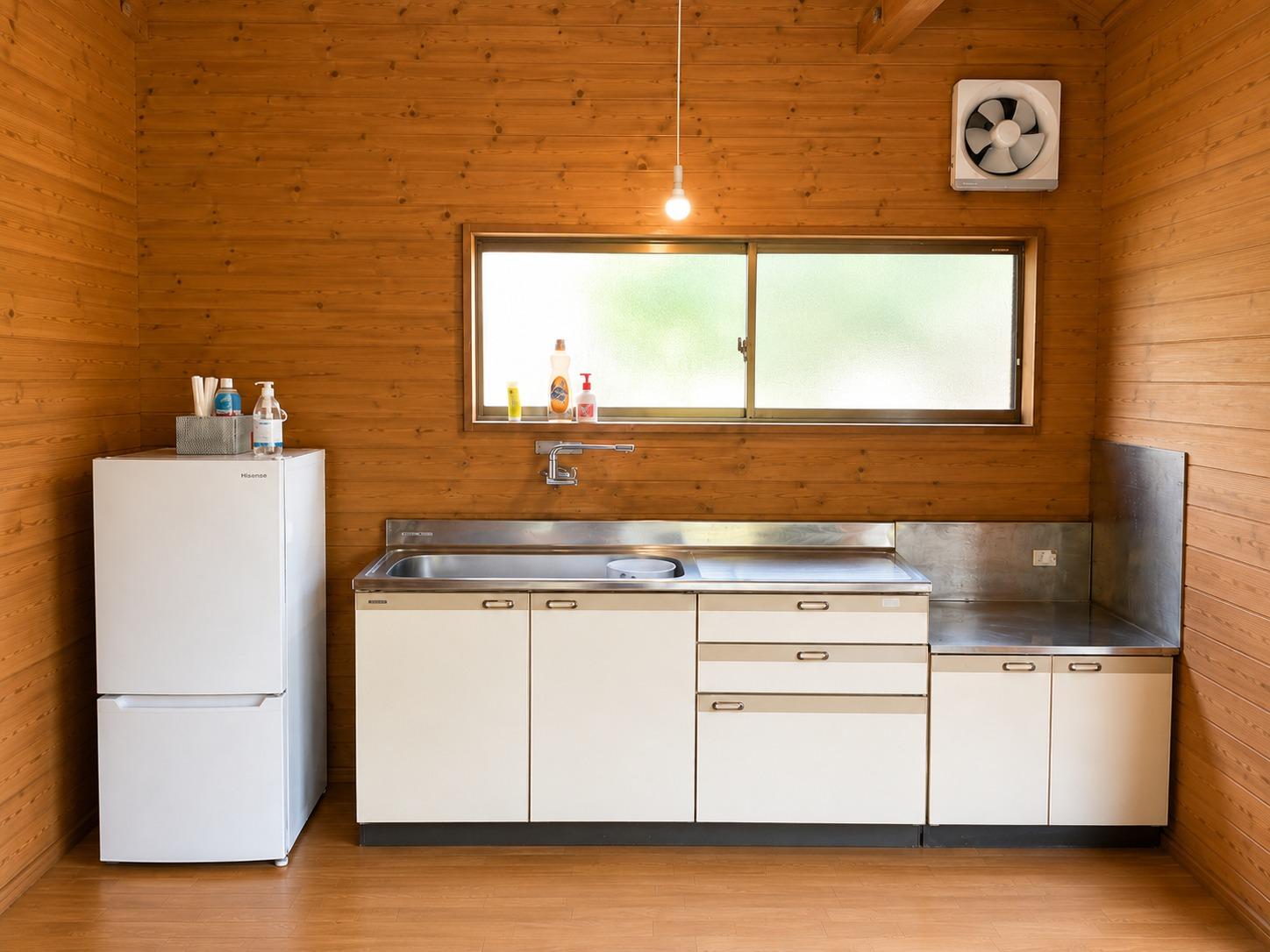 木のぬくもりを感じる大型バンガローのキッチンスペース。冷蔵庫やシンク、広い調理台を備え、自炊にも便利な設備が整っています。大きな窓から自然光が差し込み、明るく清潔感のある空間で快適にお料理をお楽しみいただけます。長期滞在やグループでのご利用にも最適です。