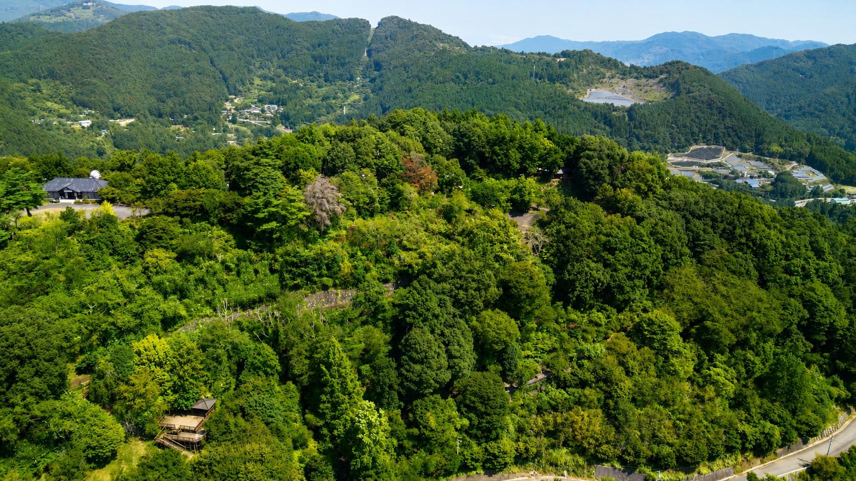 **城峯公園上空（ドローン空撮）**  上空から眺める城峯公園は、豊かな森に包まれた自然の楽園。広大な園内にはキャンプ場や遊歩道、展望スポットが点在し、四季折々の美しい景色を楽しめます。新緑や紅葉、11月には冬桜が山々を彩り、雄大な山並みとともに心癒される絶景が広がります。自然とアウトドアの魅力を一望できる、城峯公園ならではのダイナミックな空撮風景です。