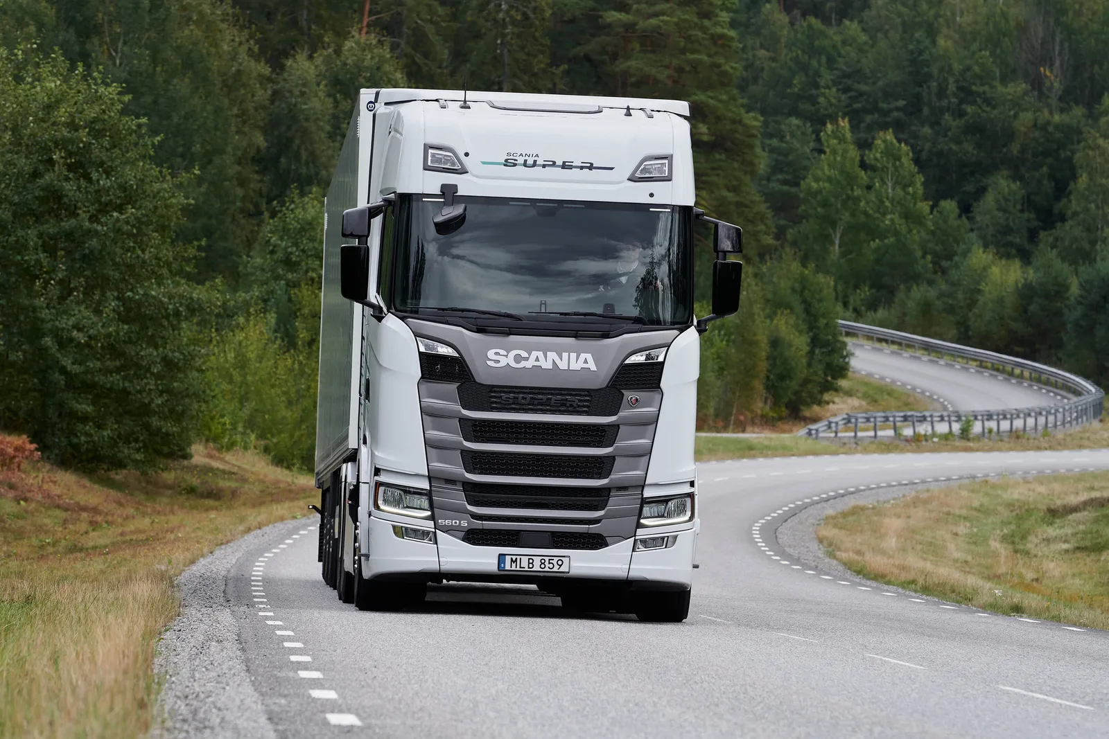 Un camion Scania bianco guida su una strada tortuosa attraverso una zona boschiva.