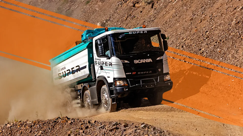 Un camion Scania Super guida su una strada sterrata, sollevando una nube di polvere.