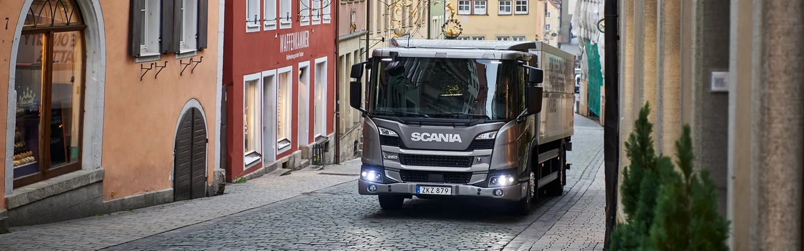 Un camion Scania guida lungo una stretta strada di città.