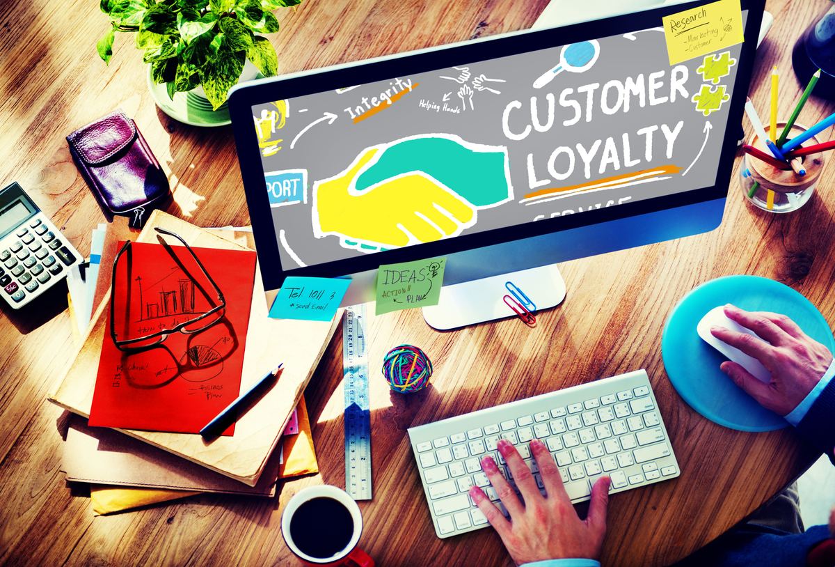 Desk with a computer screen showing the words Customer Loyalty and a handshake graphic.