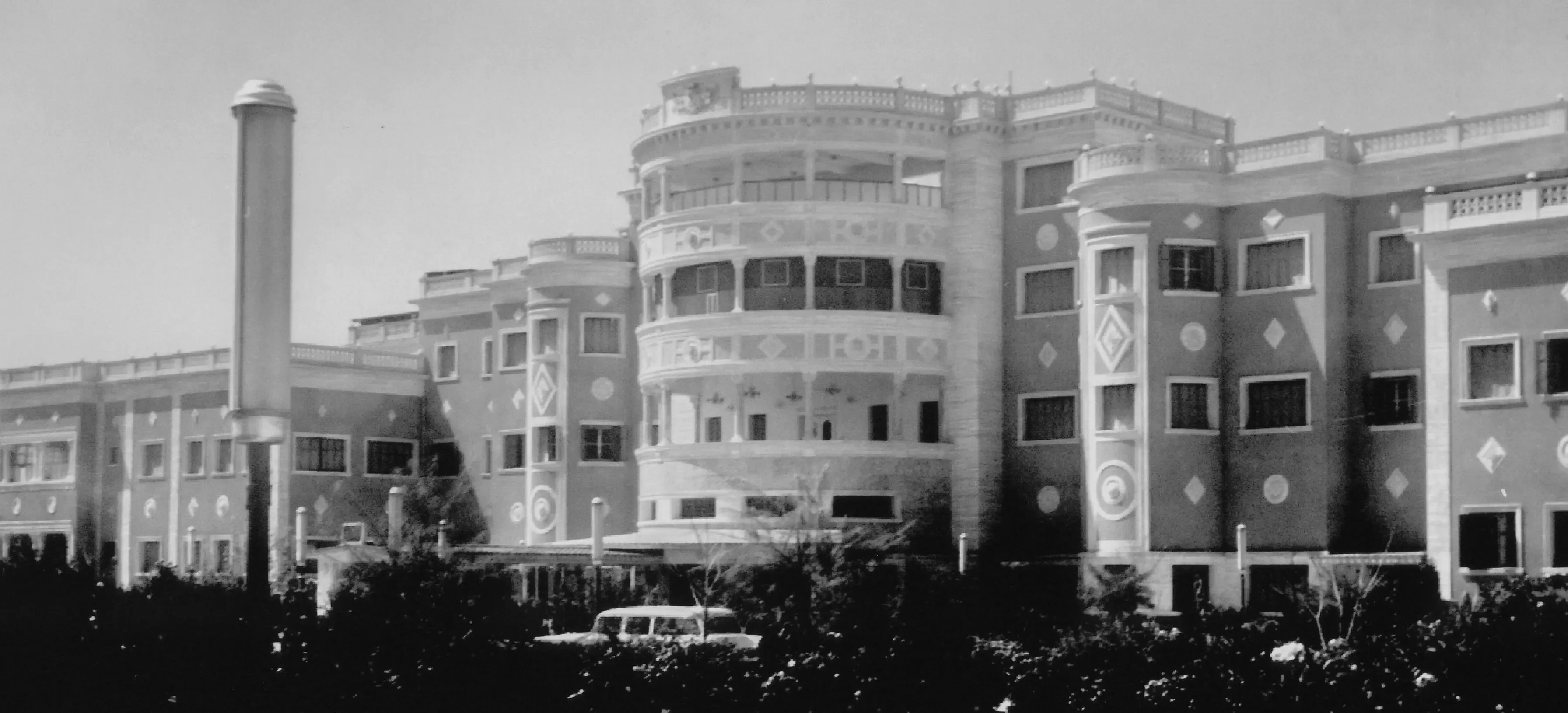 Black and white view of a grand Art Deco building with a tall chimney and rounded balconies.