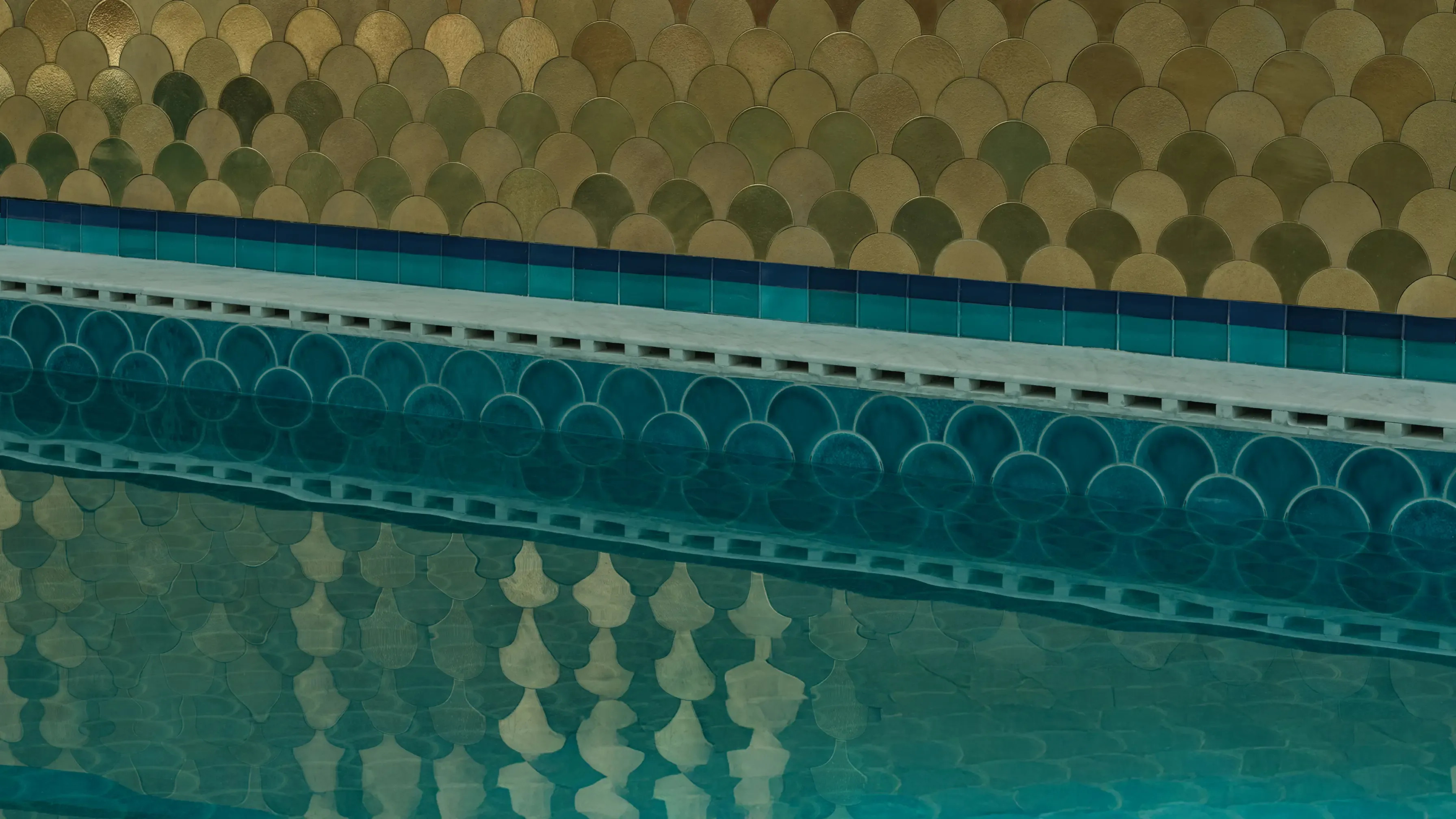Blue tiled swimming pool edge with clear water and a shimmering gold patterned wall.