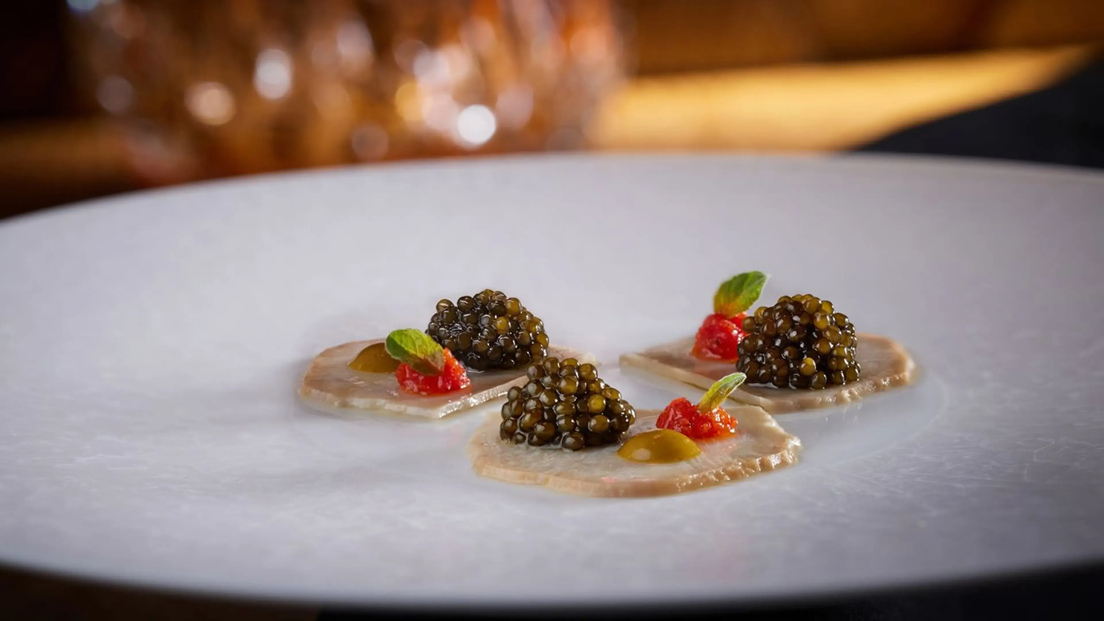 Three elegant appetizers with black caviar, red garnish, and green leaf on a white plate.