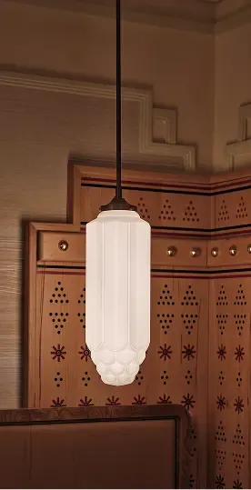 Modern cylindrical white fluted glass pendant light hanging near a patterned wooden wall panel.