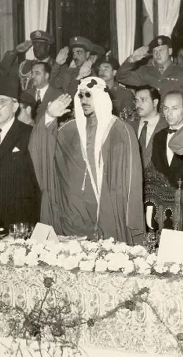 A man in traditional Arab attire salutes, surrounded by officials and soldiers.