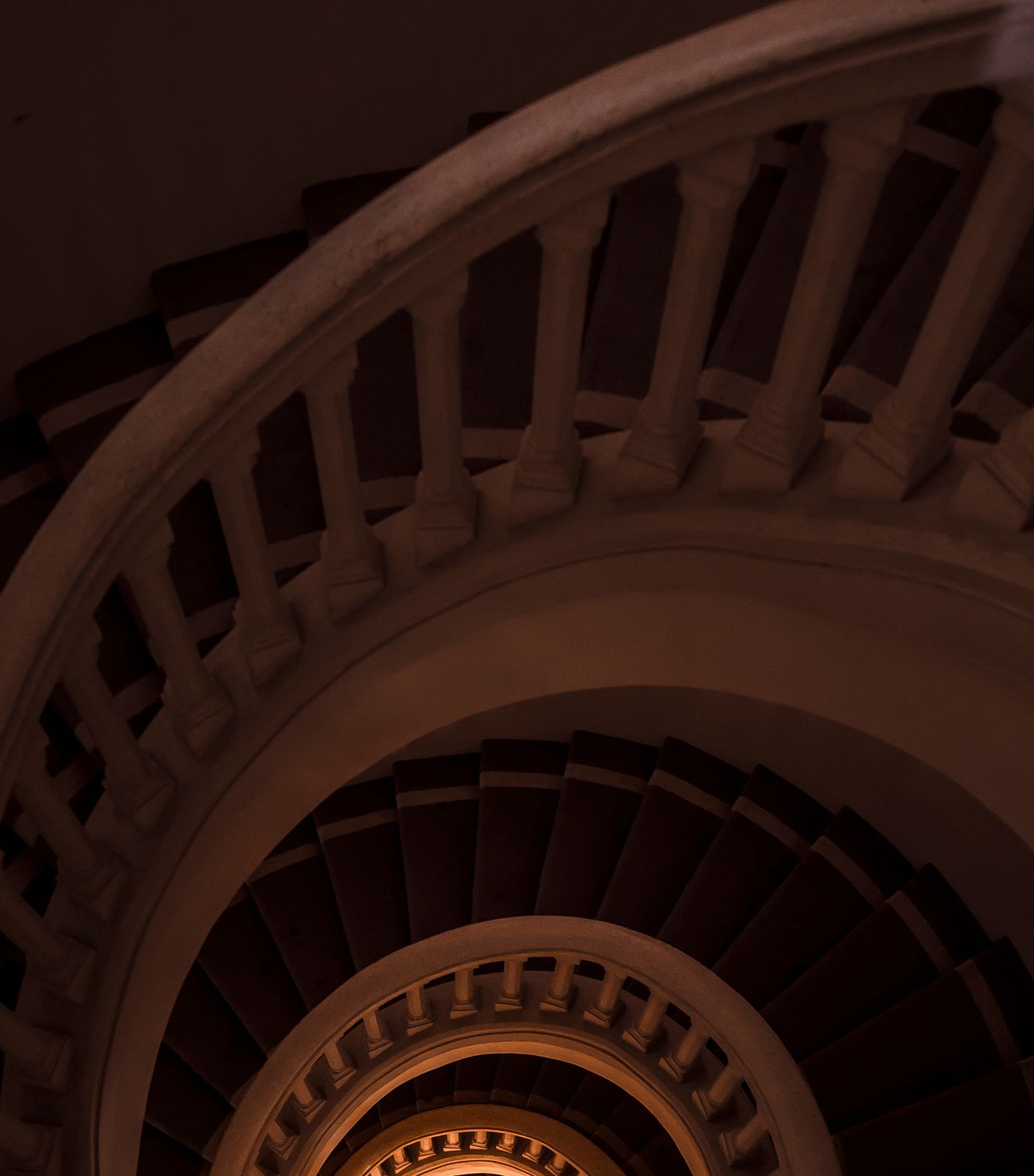Grand spiral staircase viewed from above, with ornate balustrade leading downwards.