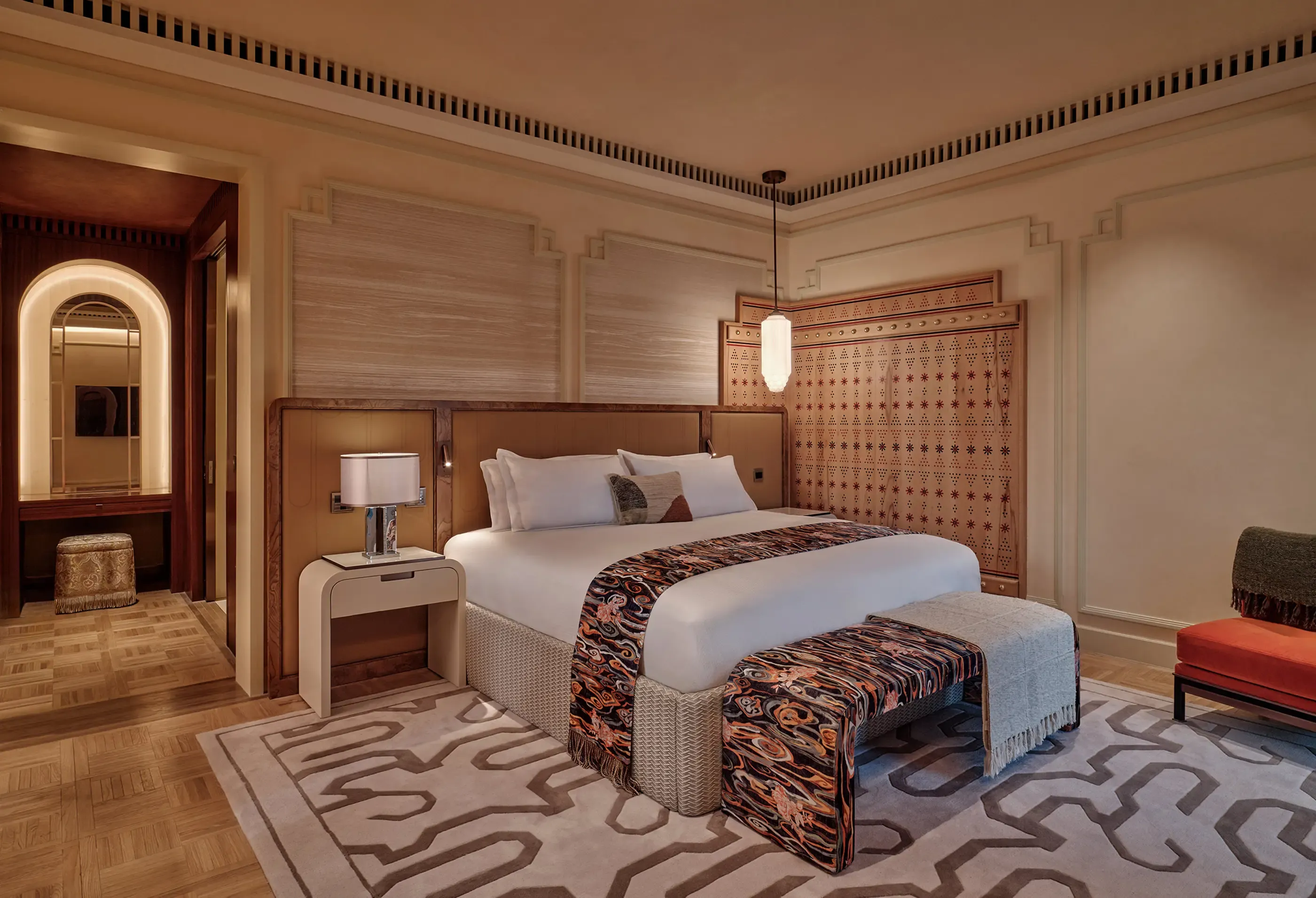 Elegant bedroom with a large bed, patterned rug, and stylish, warm-toned furnishings.