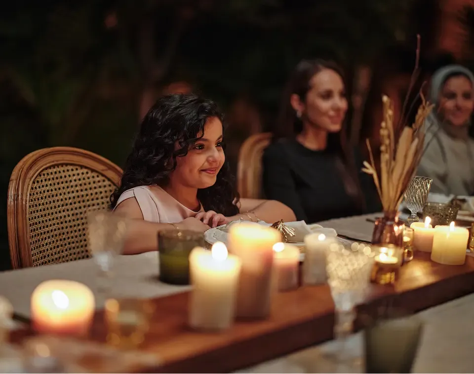 Young girl smiling at an outdoor dinner table lit by numerous flickering candles at night.