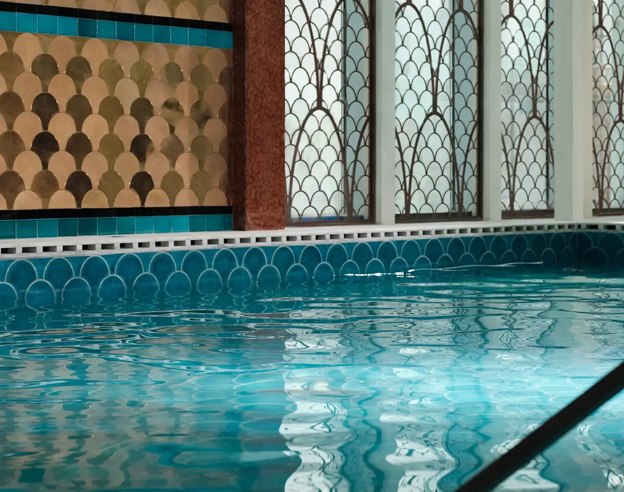 A luxurious indoor swimming pool with shimmering blue water and decorative tiled walls.