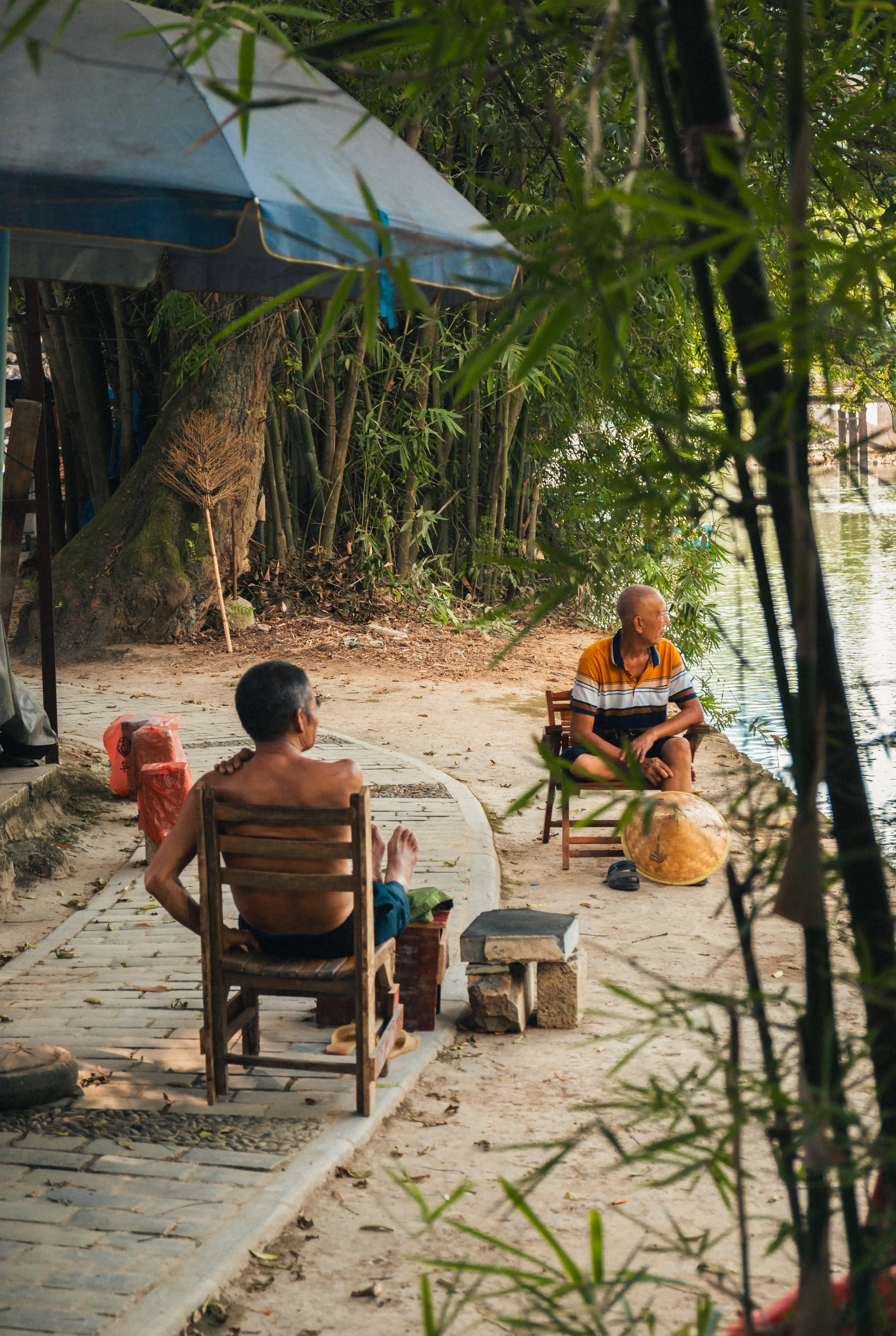 Deux hommes âgés assis au bord de la rivière Li sous un parasol bleu, Yangshuo, Chine
