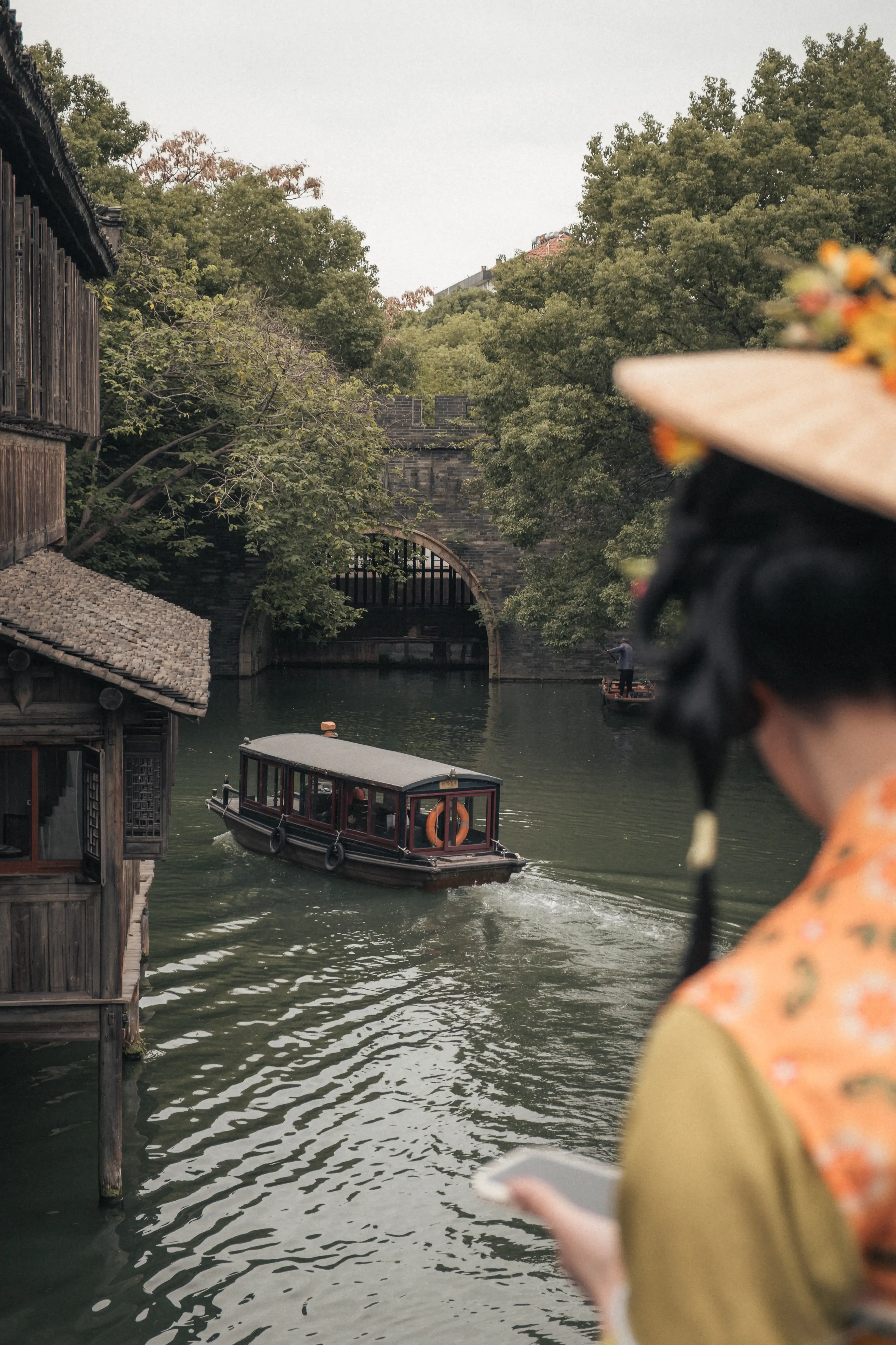 Jeune fille de dos en tenue traditionnelle verte observant une barque sur le canal depuis un pont