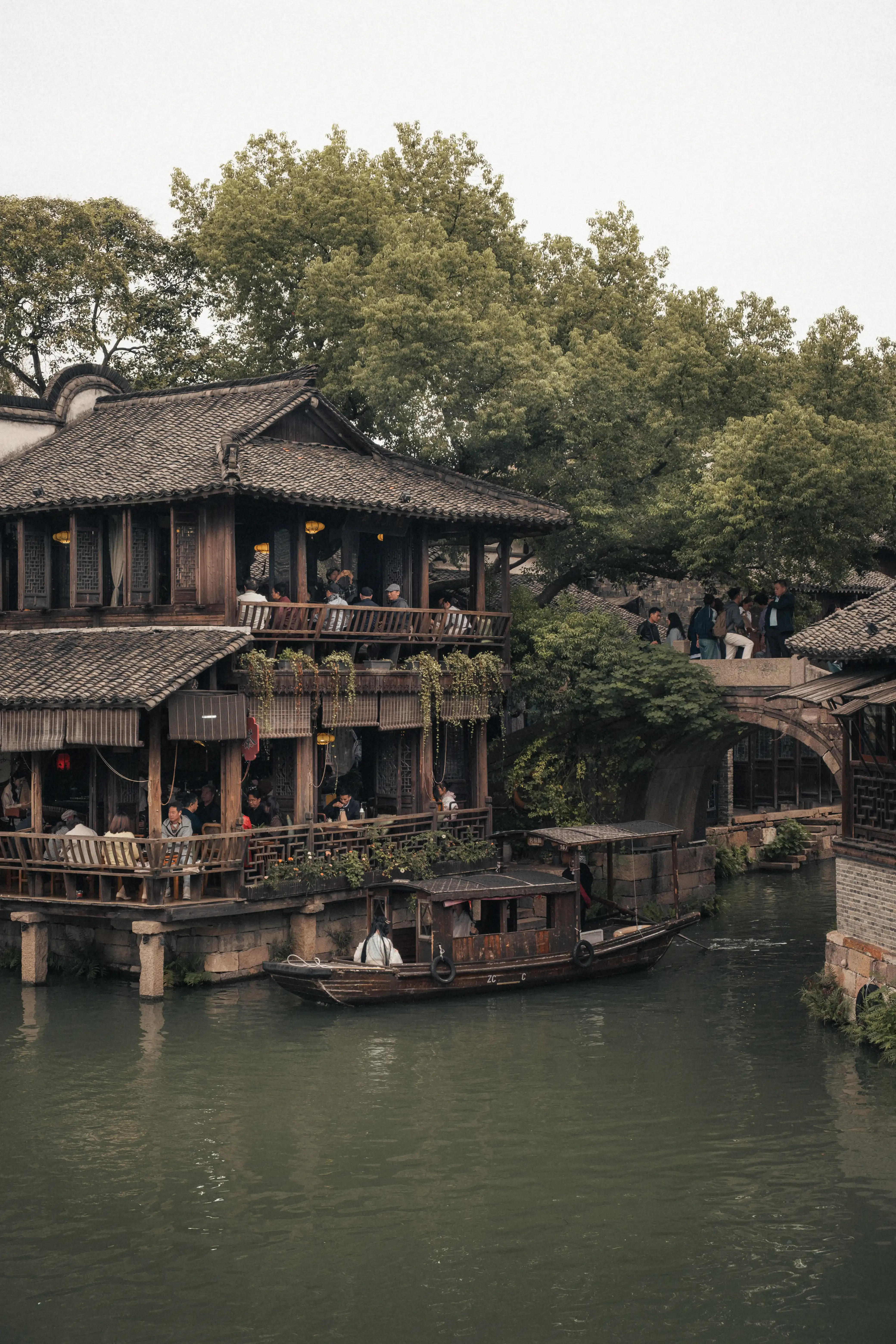 Maison de thé traditionnelle à deux étages en bois surplombant le canal vert avec des barques passant en dessous