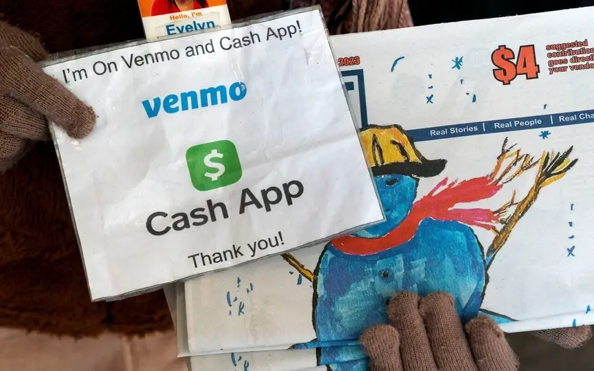 A vendor selling Street Sense, a local paper that covers issues related to the homeless and employs unhoused individuals as its vendors, holds up her sign saying she can accept donations from cashless apps like Venmo and CashApp, (AP)