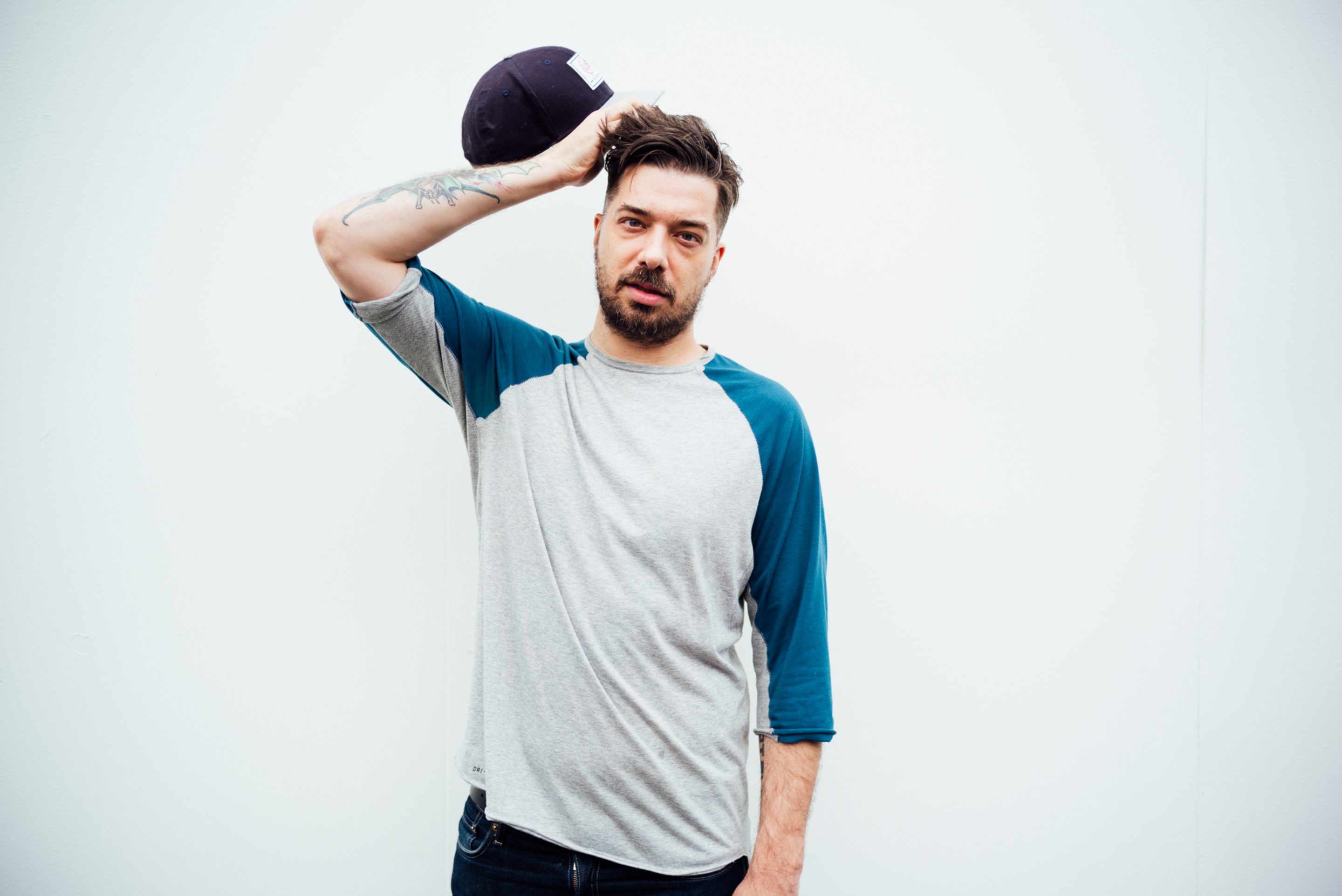 Photo of rapper Aesop Rock removing his baseball cap to scratch his head.