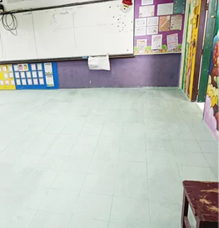 Aula con suelo claro recién embaldosado, pizarra y murales coloridos.