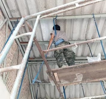Trabajador sobre andamios reparando un tejado metálico y la estructura del techo.