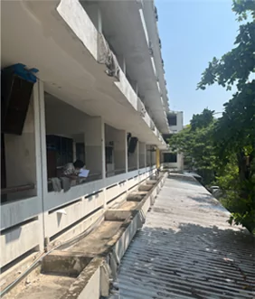 Pasillo exterior deteriorado de una escuela, con paredes de hormigón manchadas y suelo agrietado antes de la renovación.