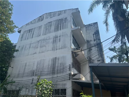 Fachada lateral de un edificio escolar blanco con manchas oscuras de humedad antes de repintarlo.