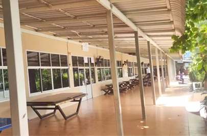 Pasillo cubierto recién pintado con paredes color crema, mesas de madera y luz solar sobre el suelo limpio.