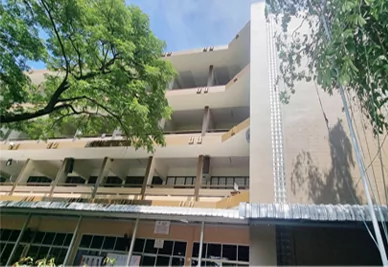 Edificio escolar de varias plantas tras el pintado, con paredes beige, balcones y árboles delante.