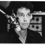 Tim Curry as Johnny LaGuardia in the WJAD studio, in the UK press kit photograph numbered 4. The text from the press kit's photo captions page: 4. TIM CURRY stars as an all-night disc jockey, who, perched in his studio high above Times Square follows and encourages the progress of the runaway girls, who thanks to his efforts become minor media celebrities.