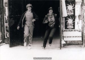 Pammy (Trini Alvarado) and Nicky (Robin Johnson) escape the Adonis Theater. TIMES SQUARE (1980) press photo 2 of 4, Germany 1982. Caption (from back): Auf der Flucht sind die beiden Teenager Nicky (ROBIN JOHNSON, rechts) und Pamela (TRINI ALVARADO) in "Times Square - Ihr könnt uns alle mal". Die beiden Mädchen werden zu wahren Helden für ihre Altersgenossen. Ein atemberaubender Film mit den Hits der letzten Jahre und einem großartigen Tim Curry als durchtriebener Disjockey Johnny LaGuardia. [On the run are two teenagers Nicky (ROBIN JOHNSON, right) and Pamela (TRINI ALVARADO) in "Times Square - You can all screw off". The two girls become true heroes for their peers. An amazing film with the hits of recent years and the great Tim Curry as cunning disc jockey Johnny LaGuardia.]