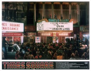 Sleez girls and boys crowd 42nd Street as Nicky performs "Damn Dog" atop the Times Square Theatre marquee. JoJo and Simon watch from the adjacent marquee with the Blondell's guitarist behind them. Text: TIMES SQUARE ™ ROBERT STIGWOOD Presents "TIMES SQUARE" EMI Starring TIM CURRY • TRINI ALVARADO And Introducing ROBIN JOHNSON Also Starring PETER COFFIELD • HERBERT BERGHOF • DAVID MARGULIES • ANNA MARIA HORSFORD Executive Producers KEVIN McCORMICK • JOHN NICOLELLA Directed by ALAN MOYLE Produced by ROBERT STIGWOOD and JACOB BRACKMAN Screenplay by JACOB BRACKMAN Story by ALAN MOYLE and LEANNE UNGER Associate Producer BILL OAKES Soundtrack available on RSO Records ond Tapes