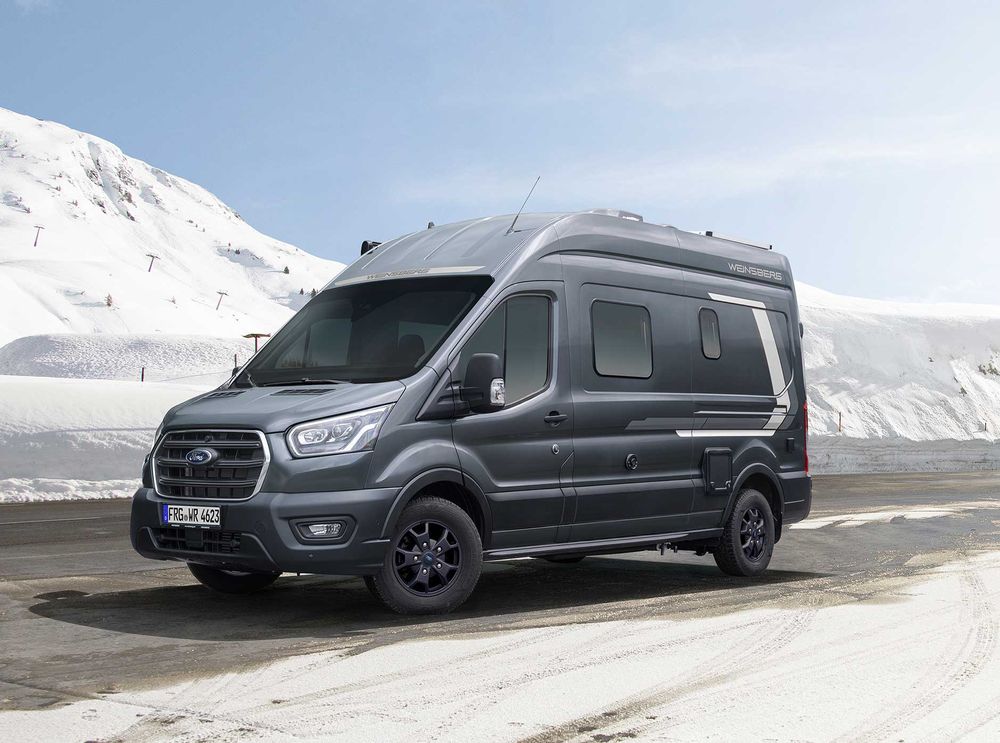 Wohnmobil auf einer Straße in hügeliger Schneelandschaft. Campingbus mieten Krefeld.