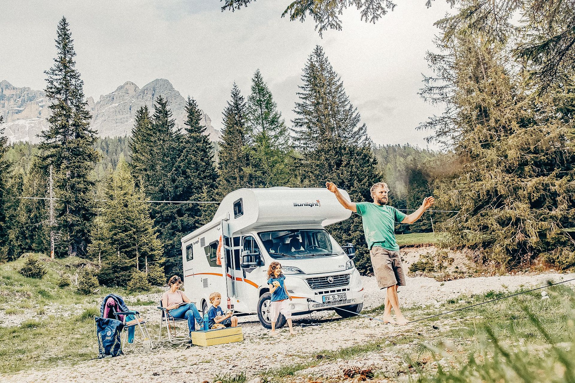 Vor dem Alkoven Wohnmobil sitzt eine Familie und hat Spaß inmitten der Natur.