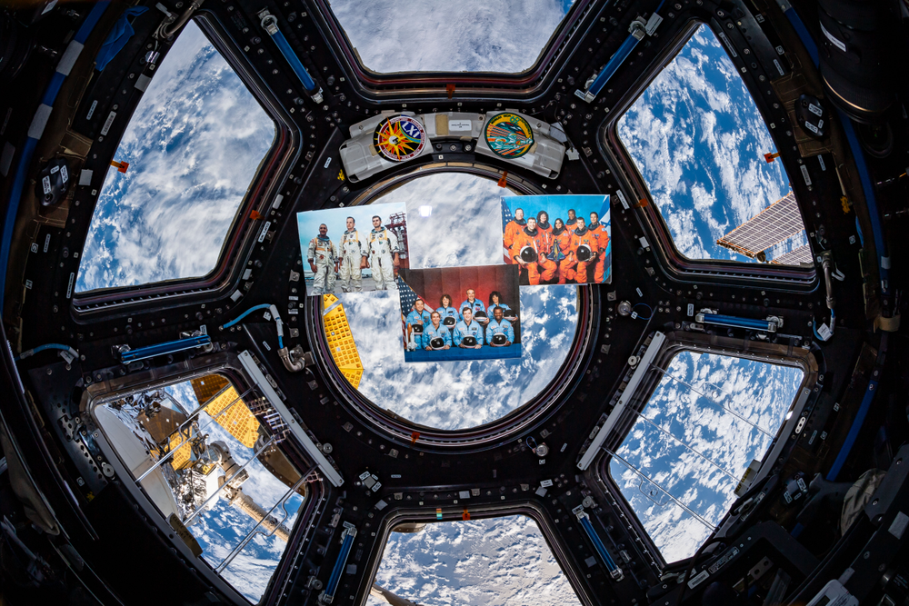 An image in the Cupola with Earth and clouds in the background and images of pictures and patches floating in space.