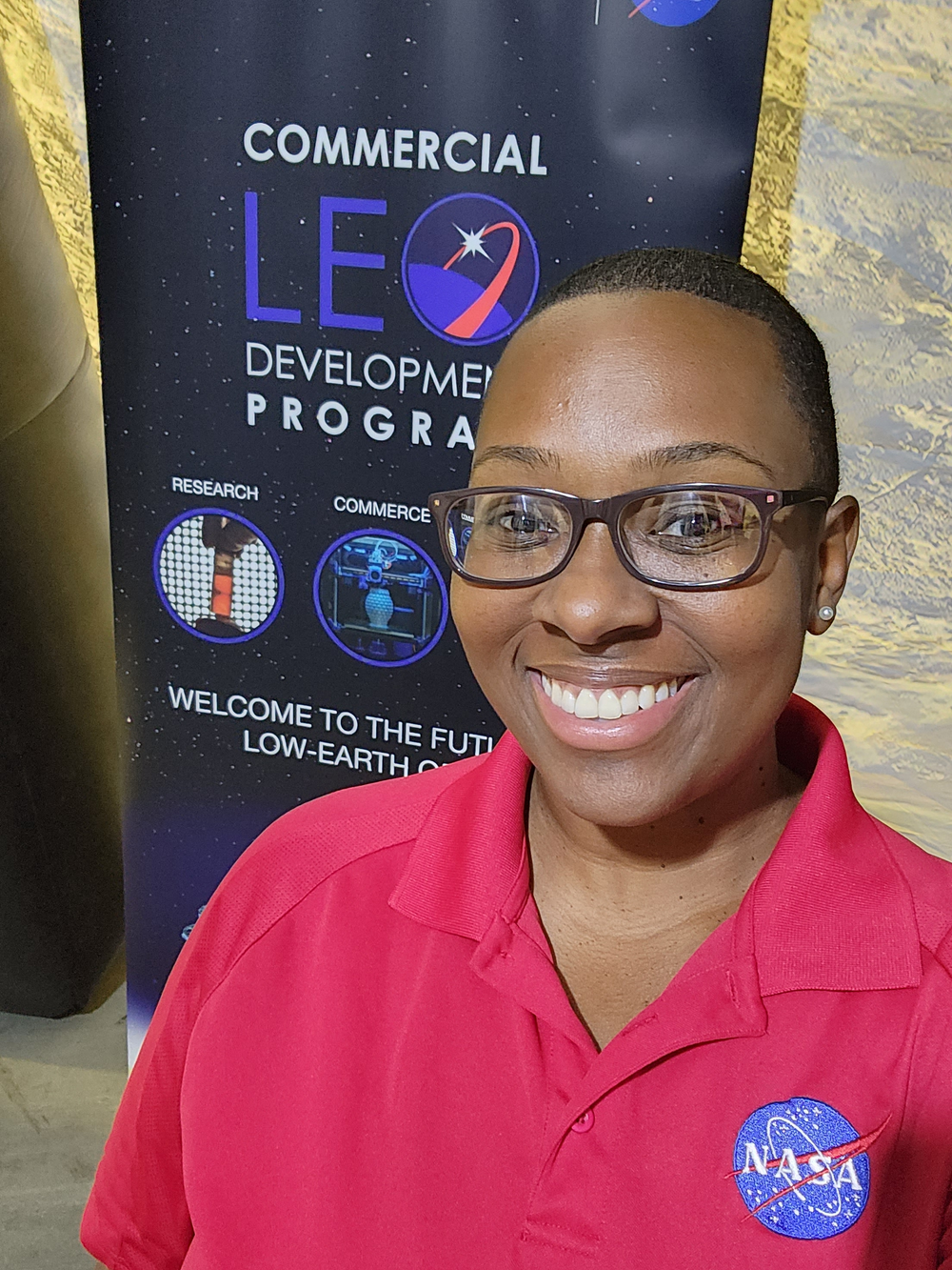 A person in a red polo wearing glasses and smiling in front of a space-themed banner.